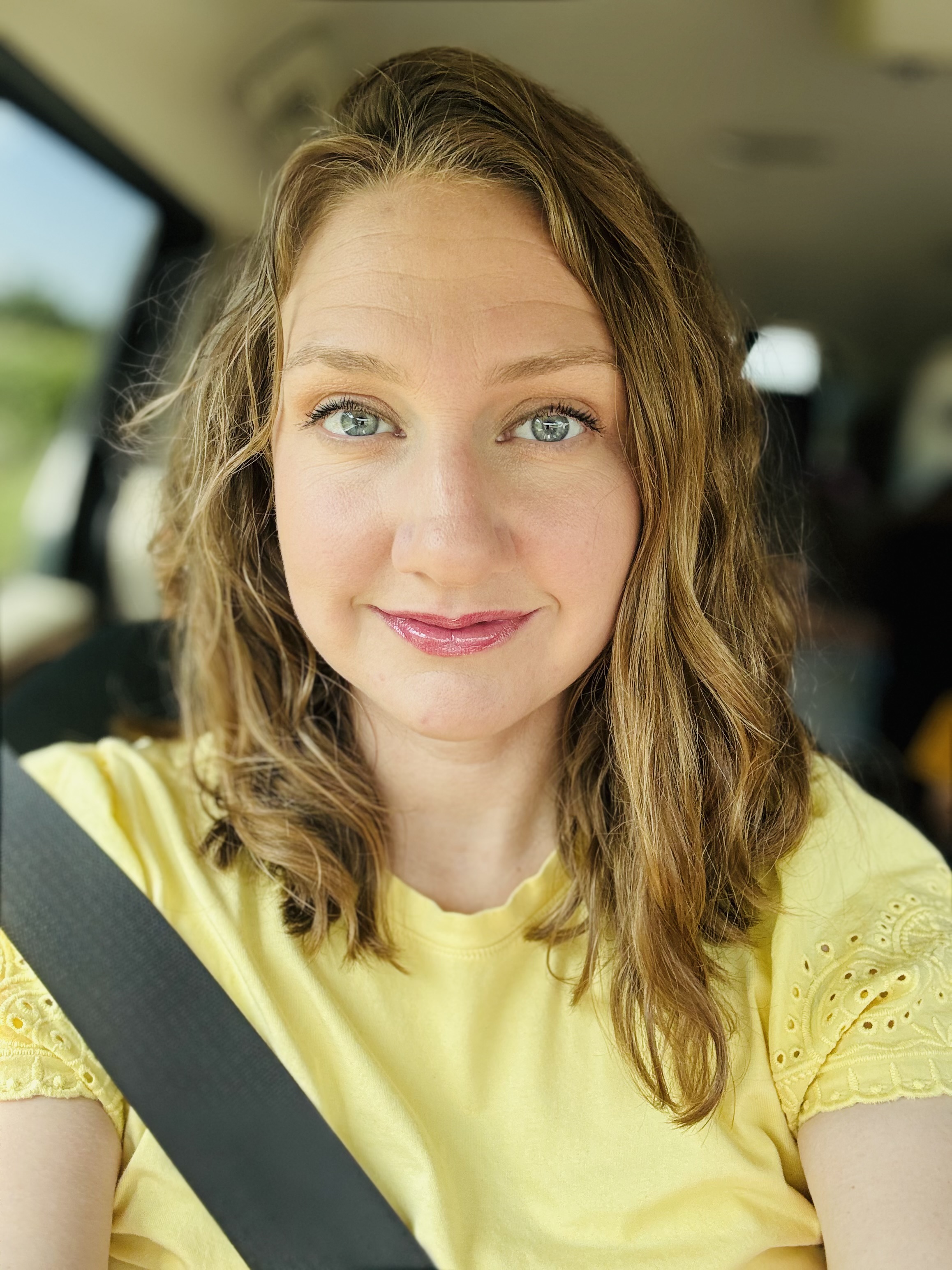 Chelsea, Foundation Coach, smiling in her car in a yellow lace top.
